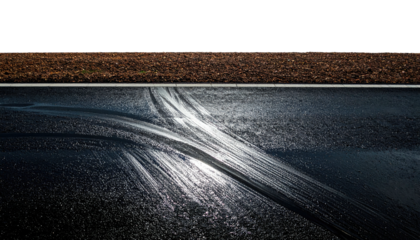 Tire tracks streak across wet asphalt below a field. Dark, moody, contrasting light