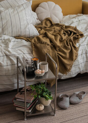 Cozy bedroom interior - metal table with coffee, books, dessert next to the disassembled bed