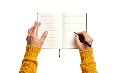Person writing in an open notebook, hands visible, wearing a yellow sweater