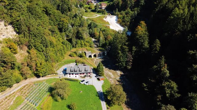 Aerial view of the Mines de Sel de Bex entrance, nestled in a valley with lush green trees and a winding path, Bex, Vaud, Switzerland.