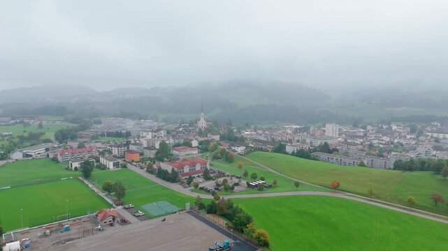 Drone orbits right over Bazenheid town and green hills in soft mist, Aerial
