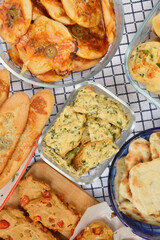 An overhead flat lay displays a festive assortment of baked savory goods, including mini pizzas, flatbreads, crackers with parsley, rolls with Parmesan and garlic, gorgonzola buns, and red pepper brea