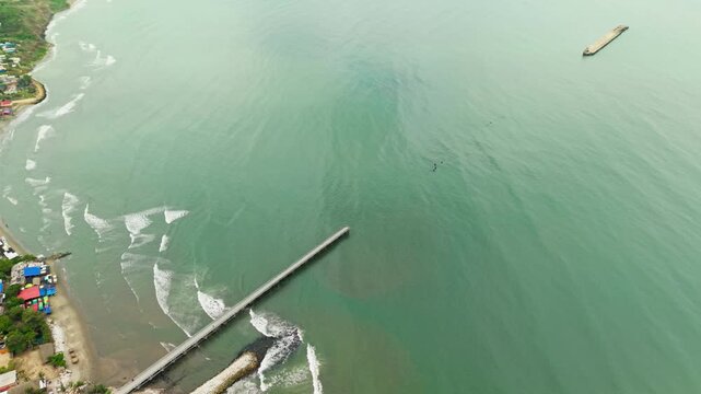 Drone view flying backwards showing the pier and coastline of puerto colombia in south america