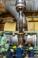 Engine room in a merchant ship features three marine engineers assembling a large piston for the main engine. 