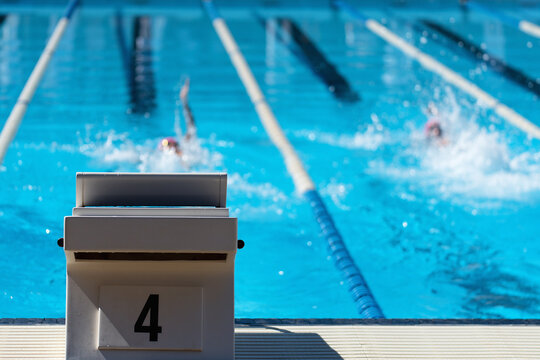 Detail of the start block with the number 4. In the background swimmers are swimming the backstroke