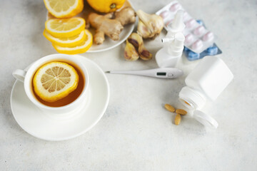 Cold and flu season treatment still life with cup of tea, lemon, pills, thermometer, nasal sprays, garlic and ginger, health and wellness concept