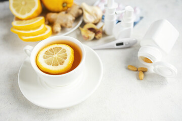 Cold and flu season treatment still life with cup of tea, lemon, pills, thermometer, nasal sprays, garlic and ginger, health and wellness concept