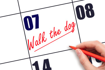 7 th day of the month.  Hand writing Walk the dog reminder and drawing a line on calendar with red...