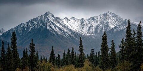Obraz premium Majestic Mountain Panorama: A breathtaking vista unfolds as towering snow-capped peaks dominate the landscape, their grandeur complemented by the verdant foreground of trees and the vast.