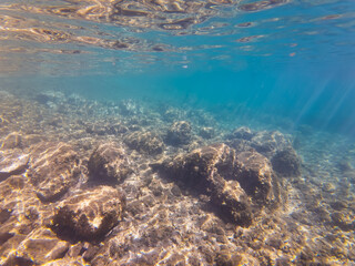 An underwater view of a rocky seabed with clear blue water and sunbeams in the Calanques National Park, Marseille.