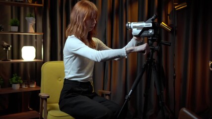 Young female filmmaker adjusting vintage camcorder on tripod - Powered by Adobe