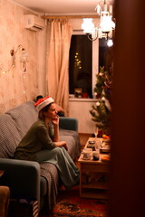 A young woman in a red New Year's hat celebrates Christmas alone at home
