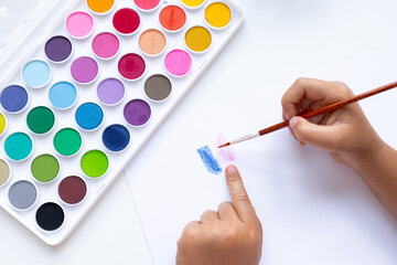 Child painting with watercolors on white paper with diverse color palette
