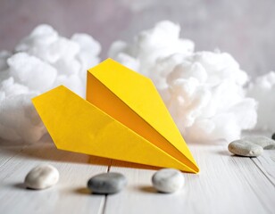 Yellow paper plane, clouds, & stones on white wood