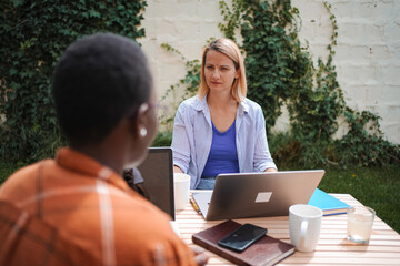 Two female colleagues working outdoors with laptops discussing a project