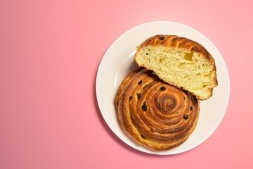 Large appetizing buns with raisins in a white plate on a pink background