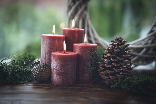 Natural christmas decoration with four burning red advent candles. Festive still life on rustic wooden table against green background and space for text.