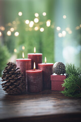 Natural christmas decoration with four burning red advent candles and a small gift. Festive still life on rustic wooden table against vertical green background with golden bokeh lights and space for t