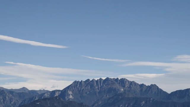 Veduta di paesaggio con monti dal profilo frastagliato sotto un cielo azzurro striato da nuvole bianche