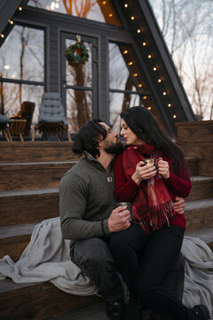 Couple enjoying cozy moments on steps of modern cabin at dusk in snowy forest setting