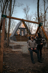 Couple enjoys a quiet moment on a swing in front of a cozy cabin in the woods during dusk