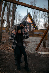 Couple enjoying a playful moment on swings near cozy cabin during twilight