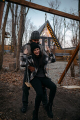 Couple enjoying a playful moment on a swing at a cozy cabin in the woods during dusk