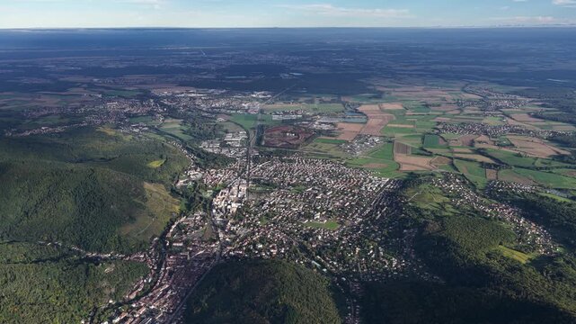 Aerial view of Thann revealing a dense cityscape nestled between lush green forests and patchwork fields under a soft, diffused sunlight, Thann, Grand Est, France.