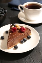 Piece of delicious chocolate cheesecake with nuts, berries and tea on black table, closeup