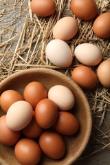 Raw chicken eggs in bowl and straw on wooden table, flat lay
