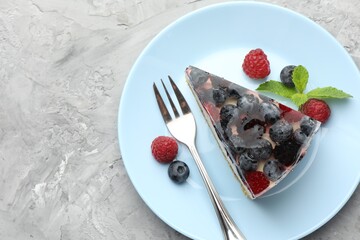 Piece of delicious cheesecake with berries, mint and fork on grey textured table, top view. Space for text