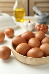 Raw chicken eggs in bowl on white table, closeup