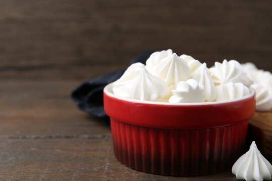 Delicious meringue cookies in bowl on wooden table, closeup. Space for text