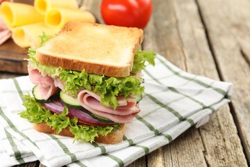 Tasty sandwich with ham and vegetables on wooden table, closeup. Space for text