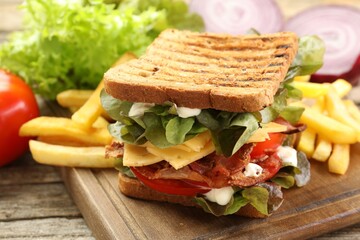 Tasty sandwich served with french fries on wooden table, closeup