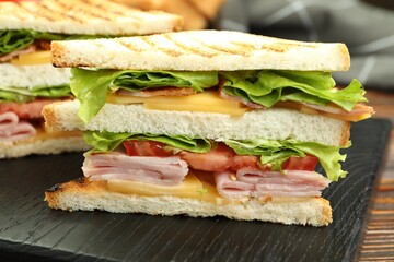 Tasty sandwiches with ham, bacon, cheese and vegetables on wooden table, closeup