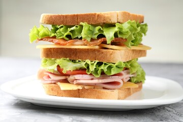 Tasty sandwich with ham, bacon, cheese and vegetables on grey textured table, closeup