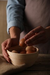 Man putting raw chicken egg into bowl at wooden table, closeup