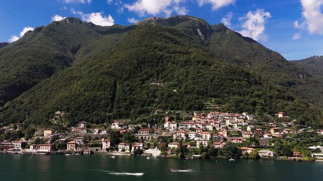 Fly sideways, view of green mountain, blue sky, houses and Lake Como