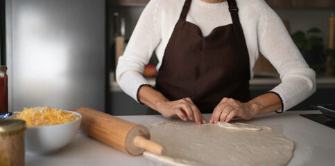 Woman's hands shaping pizza dough on a kitchen counter with ingredients nearby