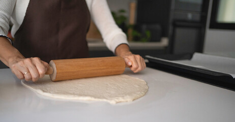 Woman's hands rolling dough on a white counter preparing baking