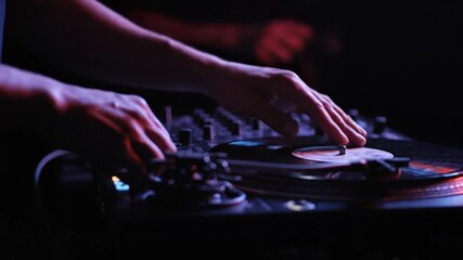 DJ performing at a nightclub with hands on turntable and mixer in low light