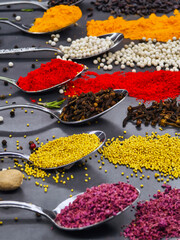Colorful spices arranged in spoons on a black surface showcasing culinary variety and texture