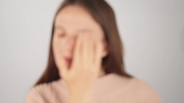 Blurred view of a tired woman taking off her eyeglasses and rubbing her eyes from digital eye strain and fatigue. Concept of poor eyesight, vision problems and overworked eyes.