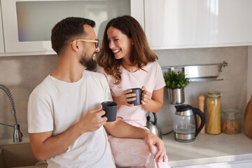 Two people share a joyful moment in a modern kitchen, holding coffee mugs while smiling at each other. They enjoy the simplicity of beginning their day together.