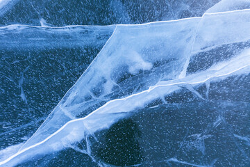 Natural winter texture of blue ice with white cracks and small bubbles in clear ice of Lake Baikal on cold winter day. Abstract textured background. Top view, Christmas layout, flat lay, close-up.