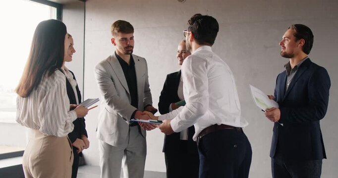 Business leader or manager shaking hands with employee in office, recognizing outstanding performance. Team of professionals standing around, applauding and celebrating colleague success together.