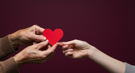Elderly hands and young hand gently holding red paper heart together for National Family Caregivers Month  