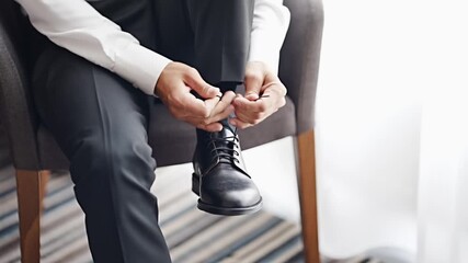 Man ties shoelaces on formal shoes in a bright room