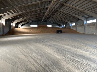 Large industrial warehouse with concrete floor and bulk grain storage under metal roof, wide interior view